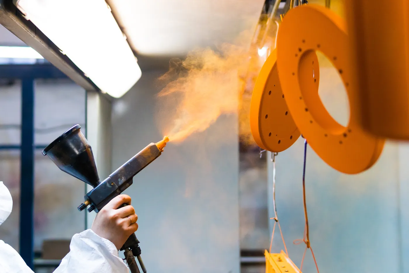 Operator powder coating metal parts with a spray gun
